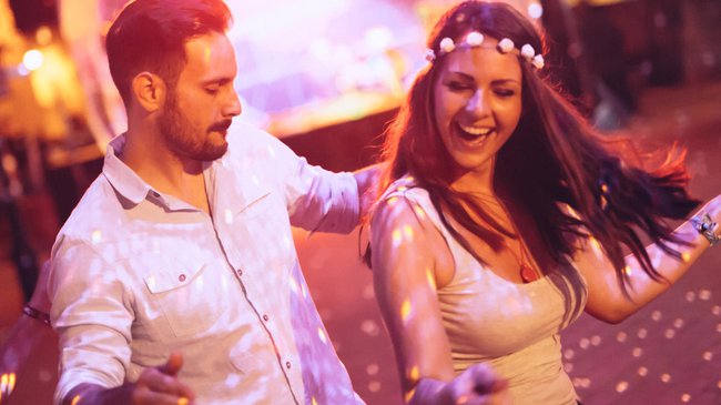 Event DJ bei einer Sommerparty. Frau mit Blumen im Haar tanzt fröhlich mit Bartmann